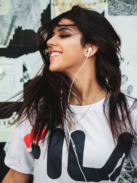 Porträt einer jungen Frau, die lächelnd Musik mit Kopfhörern hört, vor einer Graffiti-Wand.