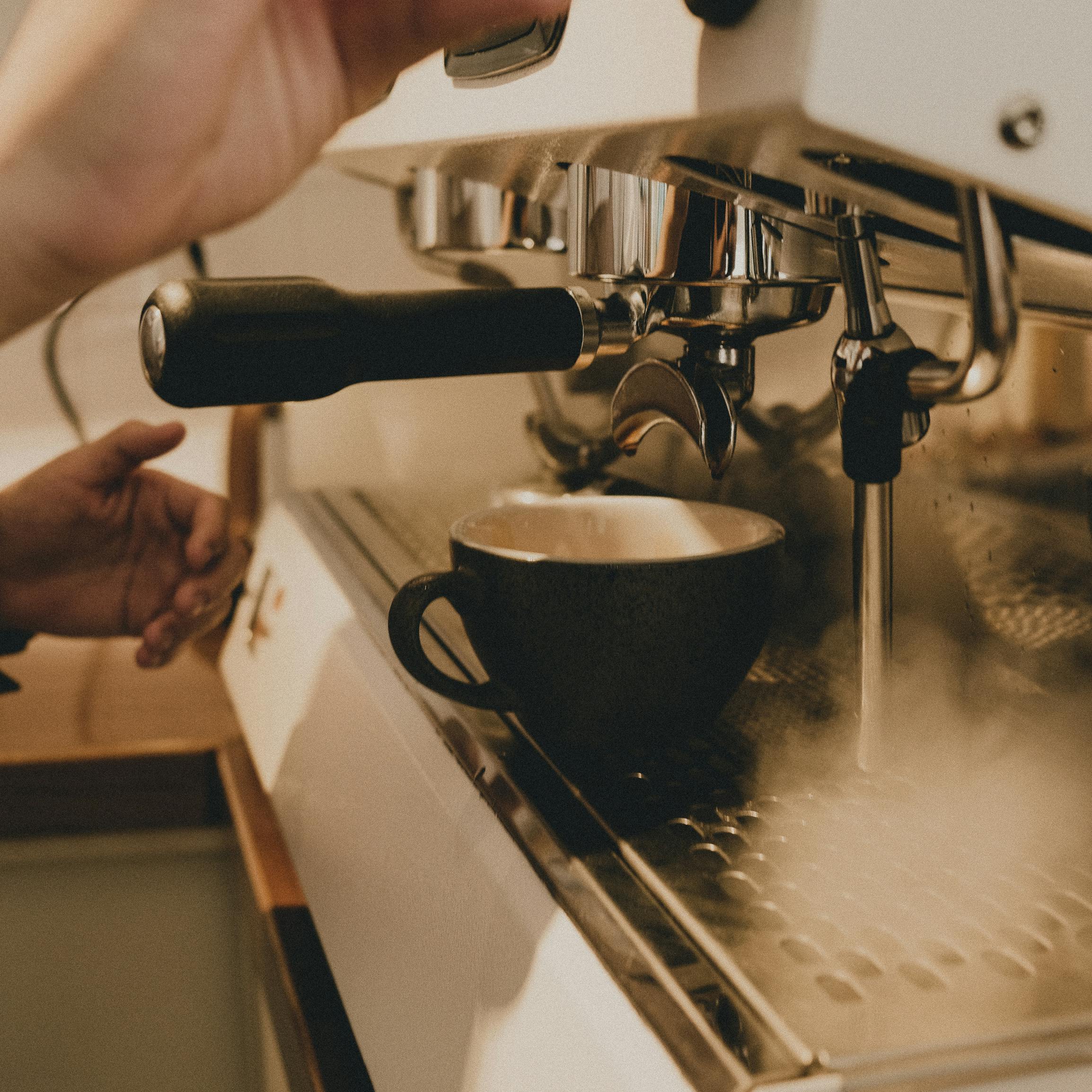 Side view of crop anonymous professional barista making coffee on professional equipment in coffee shop