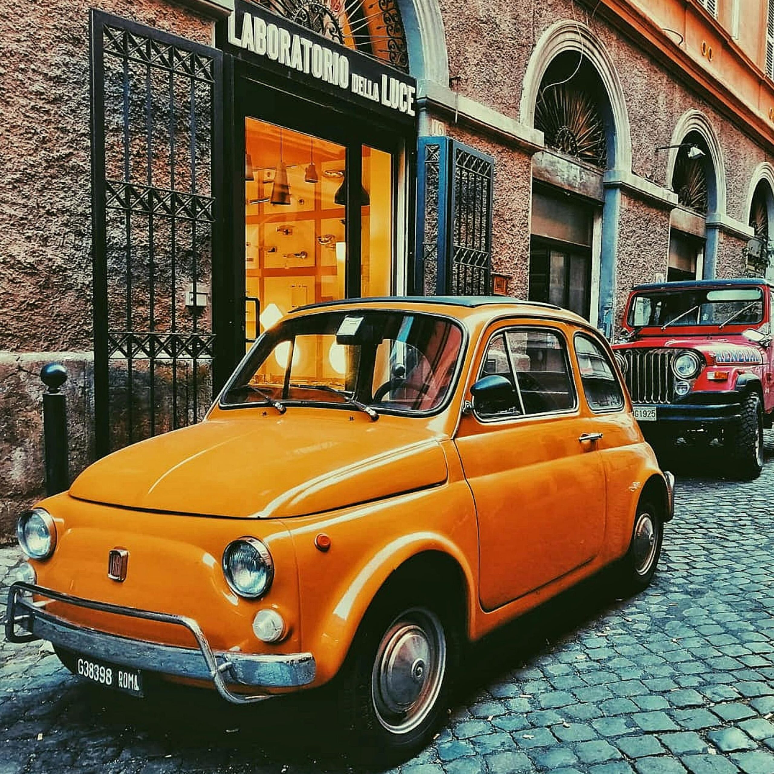 A vintage yellow Fiat car on a cobblestone street in Rome, Italy, near classic architecture.